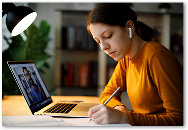 girl wearing ear buds writing in front of laptop computer