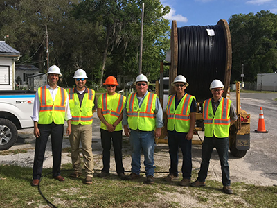 Chairman Pai with workers wearing reflective vests and hard hats in front of giant spool of fiber cable at a broadband access site in Gadsden County, Florida as part of his Digital Opportunity Tour to highlight the FCC's work to close the digital divide. Click for full size image.