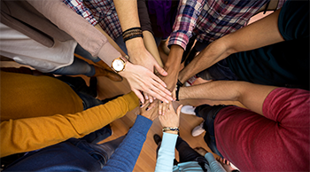 group of people layering their hands together in a circle, zoomed-in to show only arms and hands