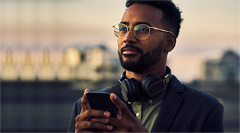 man wearing glasses, headphones around his neck, texting on phone